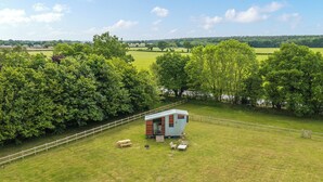 A small, modern cabin with a wooden deck and a picnic table, surrounded by lush greenery and a fenced area. - Fox Tiny House- UK47395 (Foxley, near Dereham)