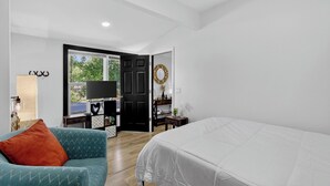 Een slaapkamer met een bed, een stoel, een bureau, een televisie en een deur die leidt naar een balkon.