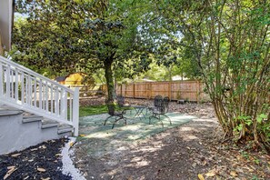 A backyard with a patio, chairs, a wooden fence, and a tree.