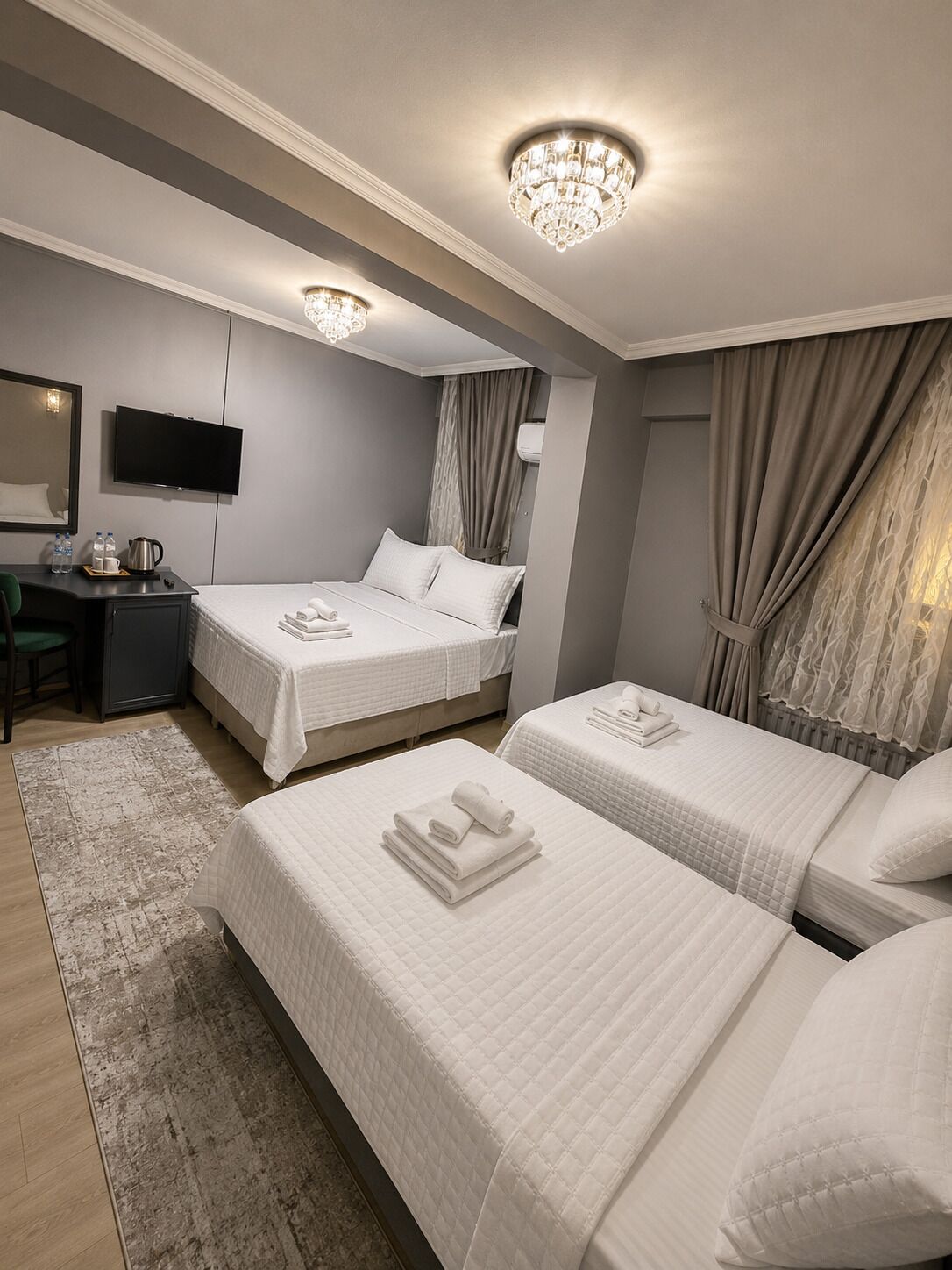 A hotel room with two beds, a desk, a TV, and a chandelier.