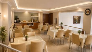A spacious dining area with multiple tables and chairs, a kitchen in the background, and a clock on the wall. - Aras Hotels Çorlu (Corlu)
