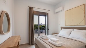 Een hotelkamer met een bed, een houten bureau, een grote spiegel en uitzicht op het buitengebied door een schuifdeur.