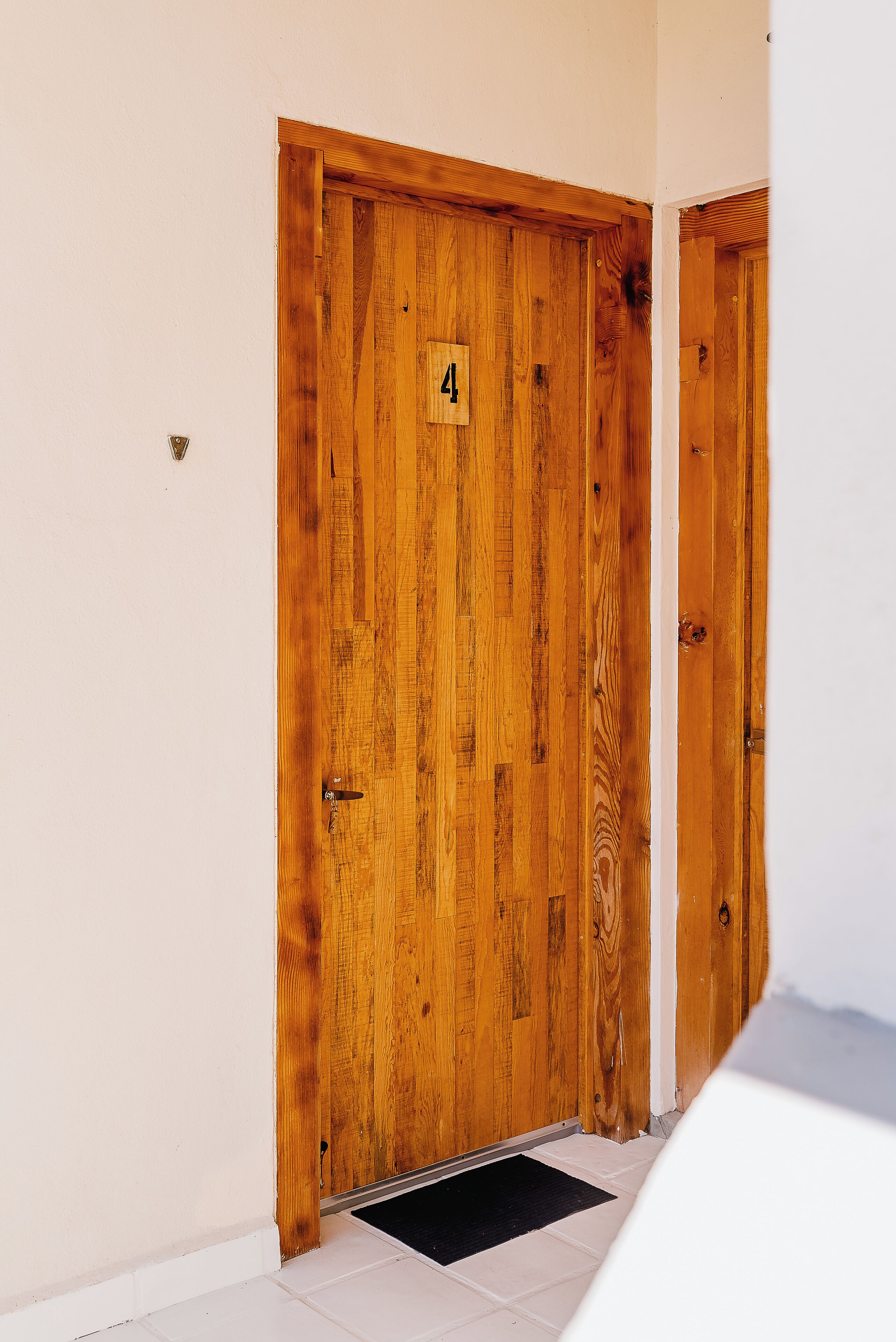A wooden door with a number plate, a white wall, and a tiled floor.