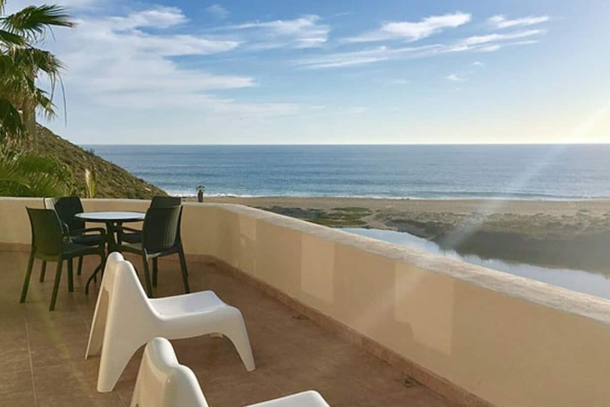 A terrace with a table and chairs, overlooking a beach and ocean.