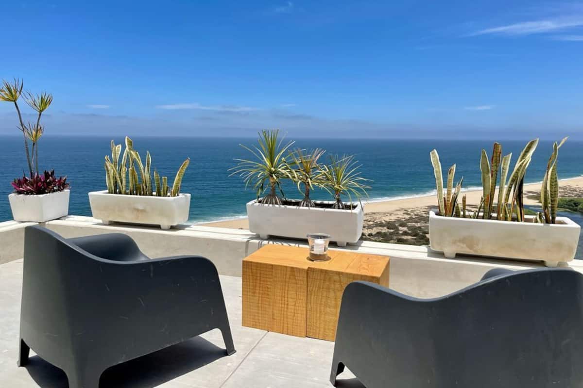 An outdoor seating area with chairs and tables, potted plants, and a view of the ocean.