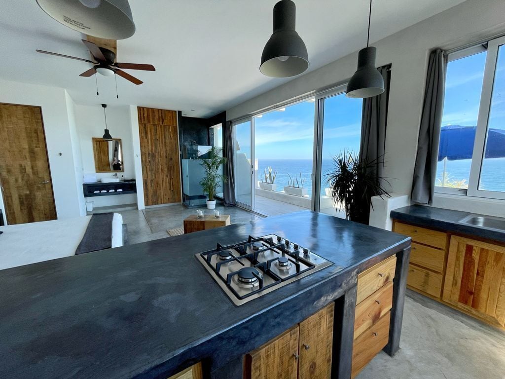 A modern kitchen with a central island, wooden cabinets, and a view of the sea.