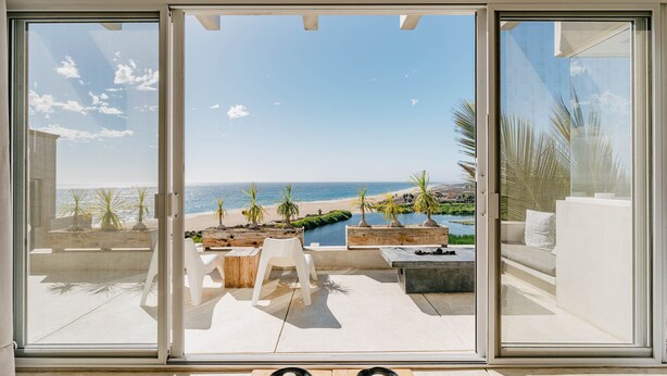 A modern room with a sliding glass door leading to a balcony with a view of the beach and ocean. - Villas La Mar (Todos Santos)