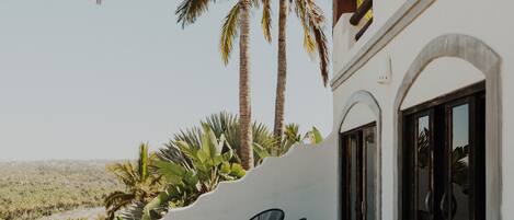 A balcony with a white wall, two black chairs, and a view of palm trees and a desert landscape.