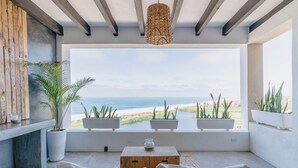 A modern room with a view of the ocean, featuring a wooden bench, a small table, and potted plants. - Villas La Mar (Todos Santos)