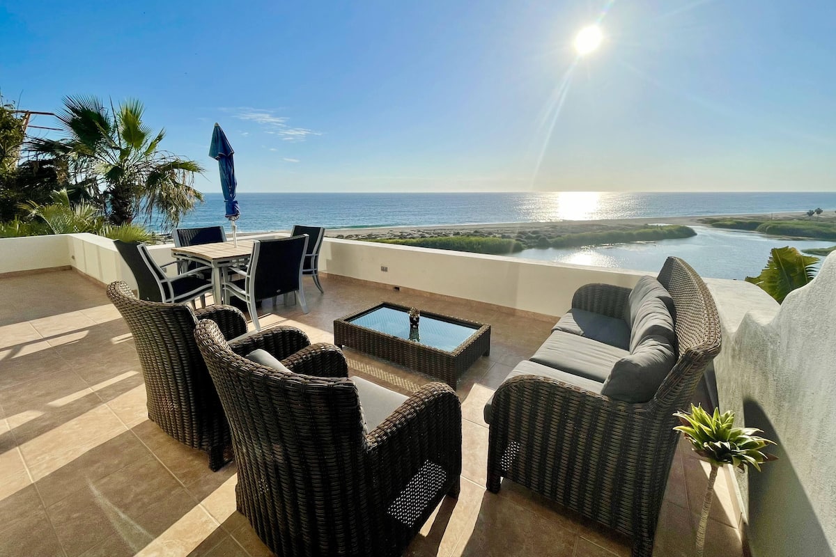 A terrace with wicker furniture, a table, and chairs overlooking a coastal view.