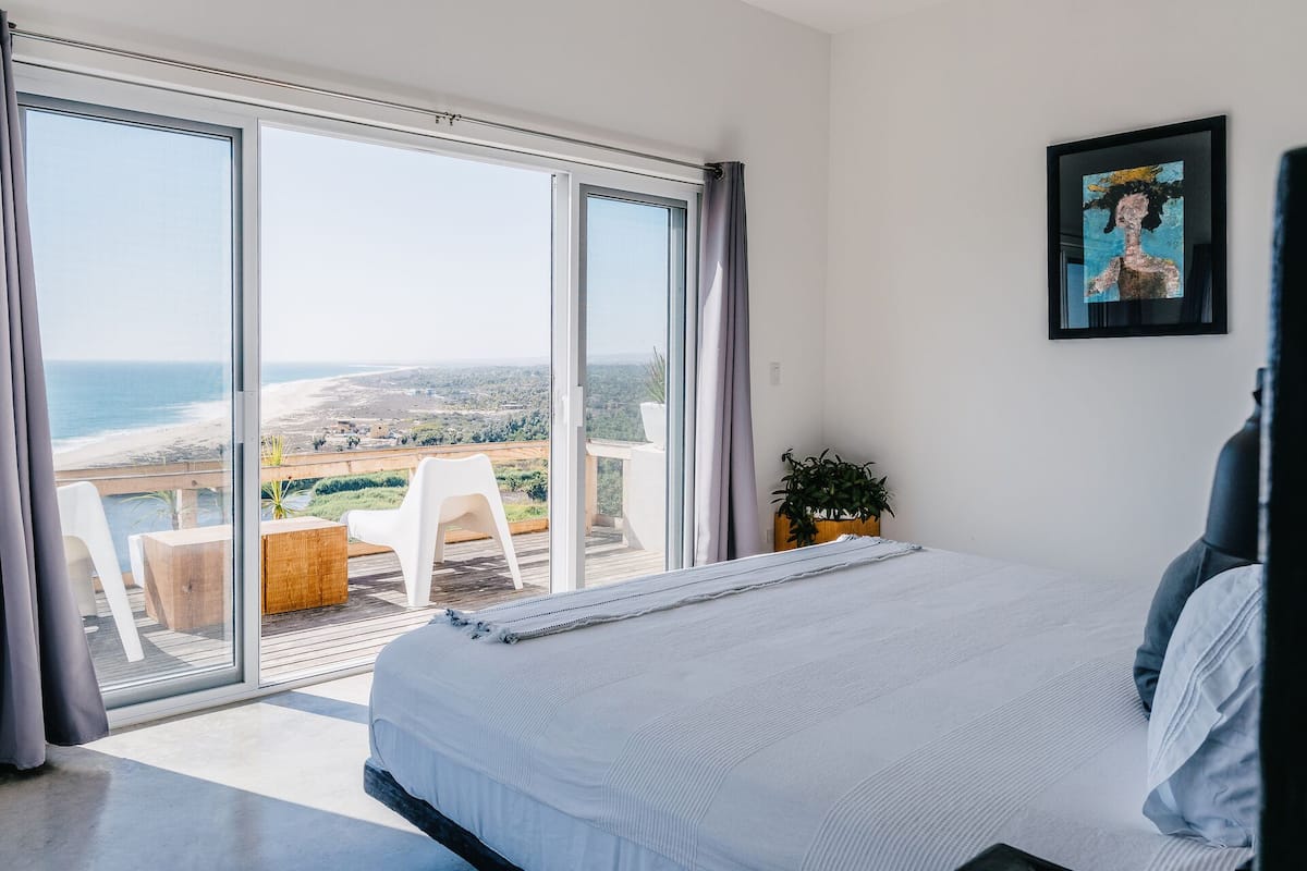 A bedroom with a large sliding glass door leading to a balcony with a view of the beach.