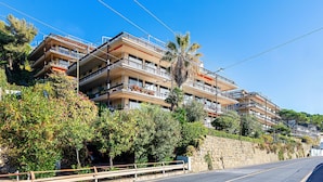 A multi-story residential building with balconies, a stone retaining wall, and lush greenery. - La Brise Apartment by Wonderful Italy (Sanremo)