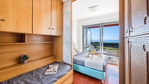 A bedroom with a large wooden wardrobe, a bed with a blue mattress, and a balcony with a view. - La Brise Apartment by Wonderful Italy (Sanremo)