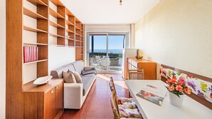 A spacious living area with a sofa, wooden shelving, a dining table, and a view through a glass door to the outdoors. - La Brise Apartment by Wonderful Italy (Sanremo)