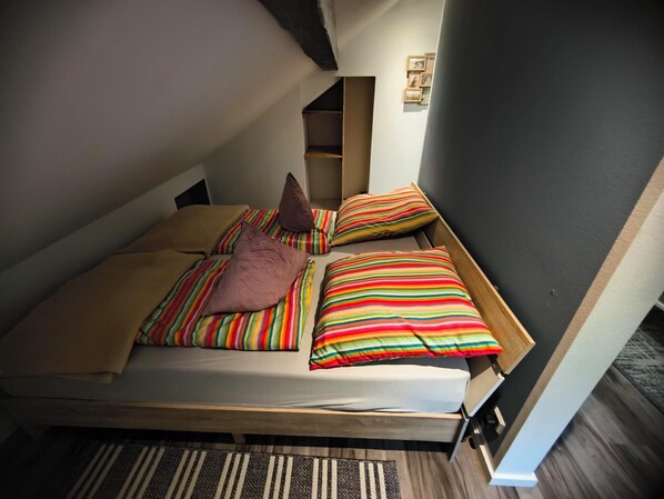 A single bed with a wooden frame, striped bedding, and two pillows.