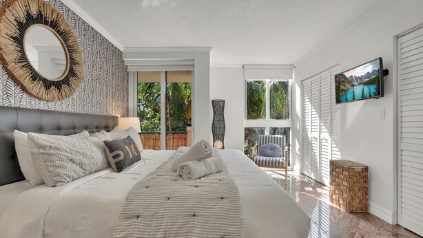 A bedroom with a large bed, a mirror, a television, and a view of the outdoors. - Treetop Retreat Cozy 2 Bedroom in Grove (Miami)