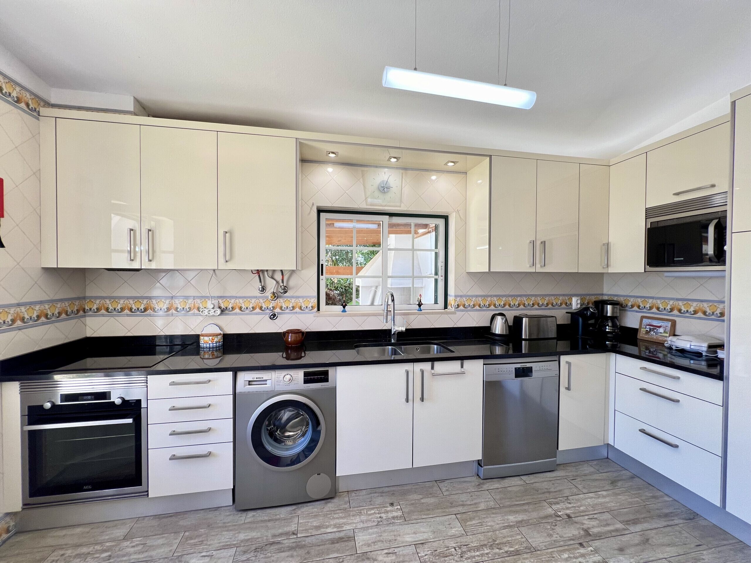 A modern kitchen with white cabinets, a built-in oven, a washing machine, and a microwave.