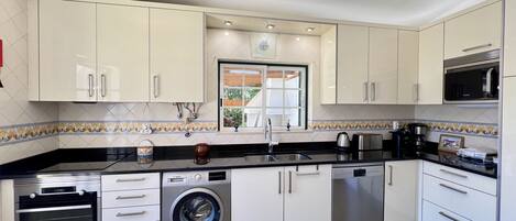 A modern kitchen with white cabinets, a built-in oven, a washing machine, and a microwave.