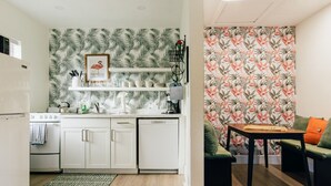 A compact kitchen with white cabinets, a built-in oven, and a microwave. There is a wooden dining table with a chair and a green sofa with orange cushions.