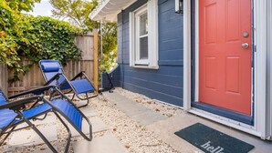A house with a red door, a blue exterior, and a covered patio area with blue chairs.