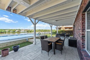 Eine überdachte Terrasse mit Gartenmöbeln, einem Pool und Blick auf ein Gewässer.
