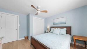 A bedroom with a bed, a ceiling fan, a bedside table with a lamp, a wooden bench, and a door. - Cozy Beach Haven Terrace Home, 1 Block From Beach, Restaurants & Wawa! (Long Beach)
