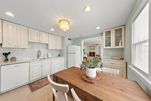 Una cocina con armarios blancos, una mesa de comedor de madera e iluminación empotrada.