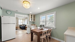 A kitchen with a dining table, chairs, a refrigerator, a clock, and a window with blinds. - Cozy Beach Haven Terrace Home, 1 Block From Beach, Restaurants & Wawa! (Long Beach)