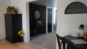 A modern living room with a dark fireplace, a 'hello' sign, a 'welcome' sign, and a guest book on a desk. - Spacious Ranch w/Hot Tub & Game Room, Sleeps 14! (Greeley)