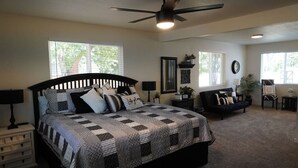 A bedroom with a large bed, a ceiling fan, and two windows. - Spacious Ranch w/Hot Tub & Game Room, Sleeps 14! (Greeley)