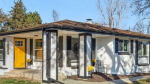A single-story house with a yellow front door, a small porch with two chairs, and a chimney. - Spacious Ranch w/Hot Tub & Game Room, Sleeps 14! (Greeley)