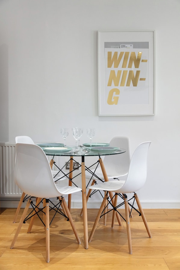 Un coin repas avec une table en verre, des chaises blanches et une affiche encadrée accrochée au mur.