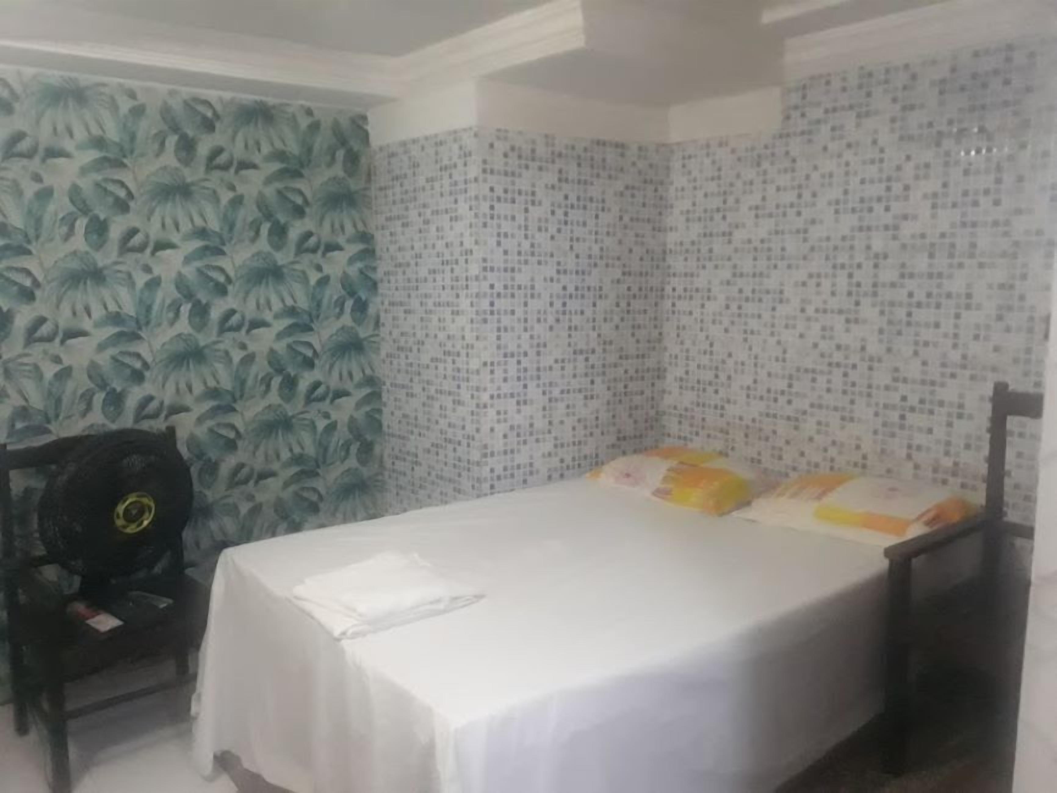 A room with a bed, a chair, and a wall with a leaf pattern.