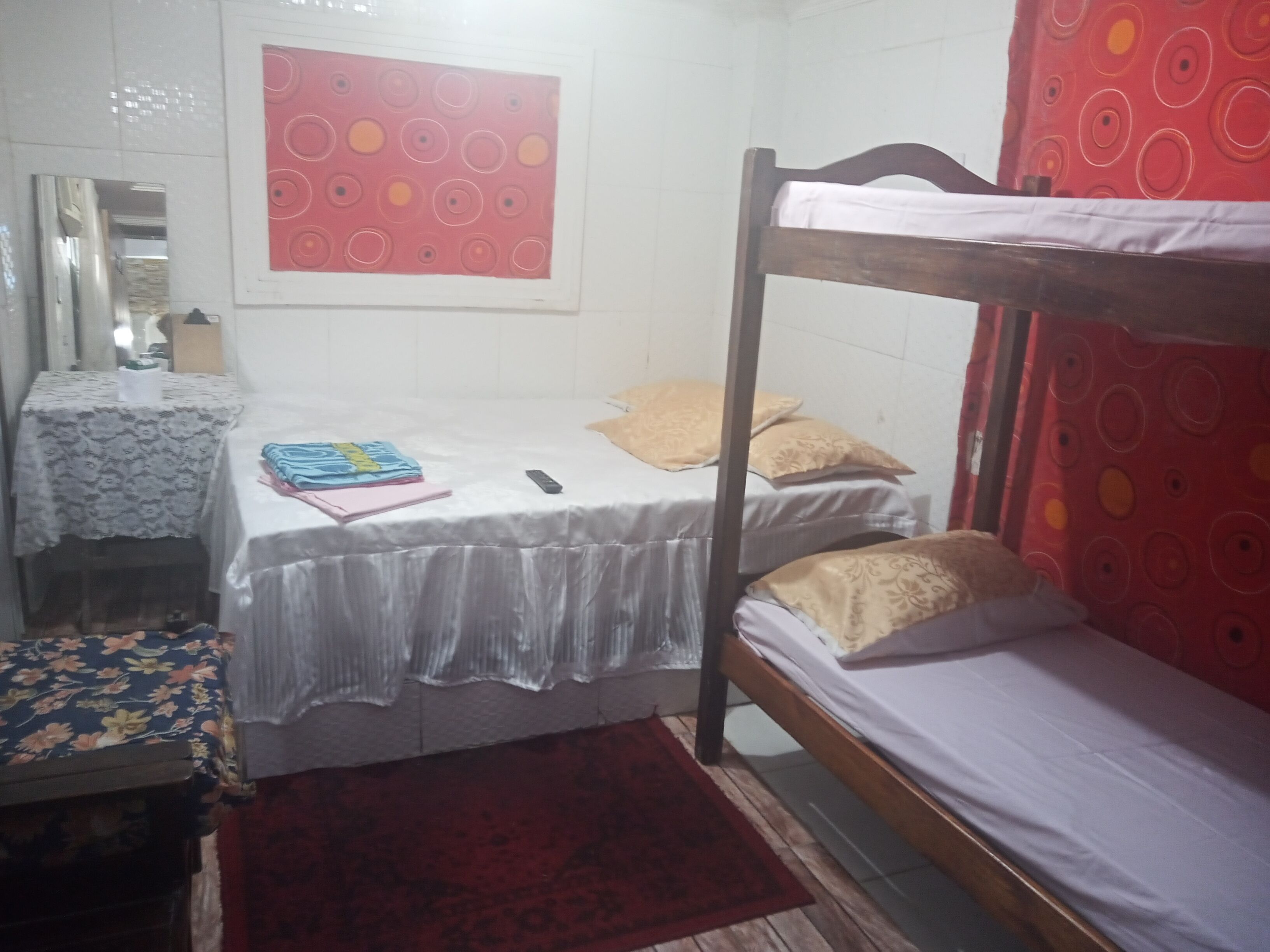 A small, single-room accommodation with a bunk bed, a small table with a patterned tablecloth, a red curtain, and a mirror on the wall.