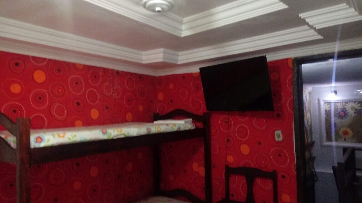 A room with a bunk bed, a flat-screen TV mounted on the wall, and a patterned red wall.