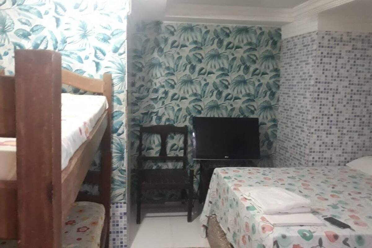 A bedroom with a bunk bed, a single bed, a television, and patterned wallpaper.
