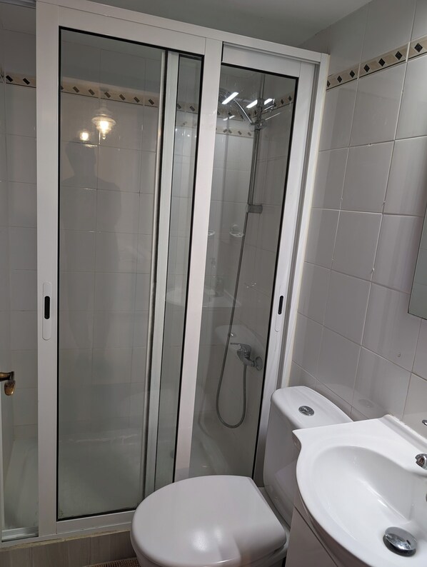 Une salle de bain avec une douche à parois de verre, des toilettes blanches et un lavabo.
