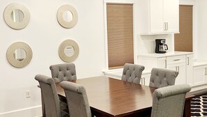 Un coin repas comprenant une table en bois et quatre chaises rembourrées, des meubles blancs et des miroirs décoratifs accrochés au mur.