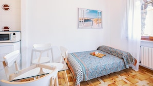 A small, bright room with a bed, a chair, a table, and a microwave. - Silent Apartment by Wonderful Italy (Sanremo)