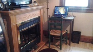A living room with a fireplace, a television, a laptop on a table, and a chair. - Relax in our Ladies & Gents Room at The Cobblestone Bed & Breakfast (Birchwood)