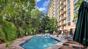 A swimming pool surrounded by lounge chairs and umbrellas, with a building in the background. - Relaxing Condo with Free Parking (Miami)