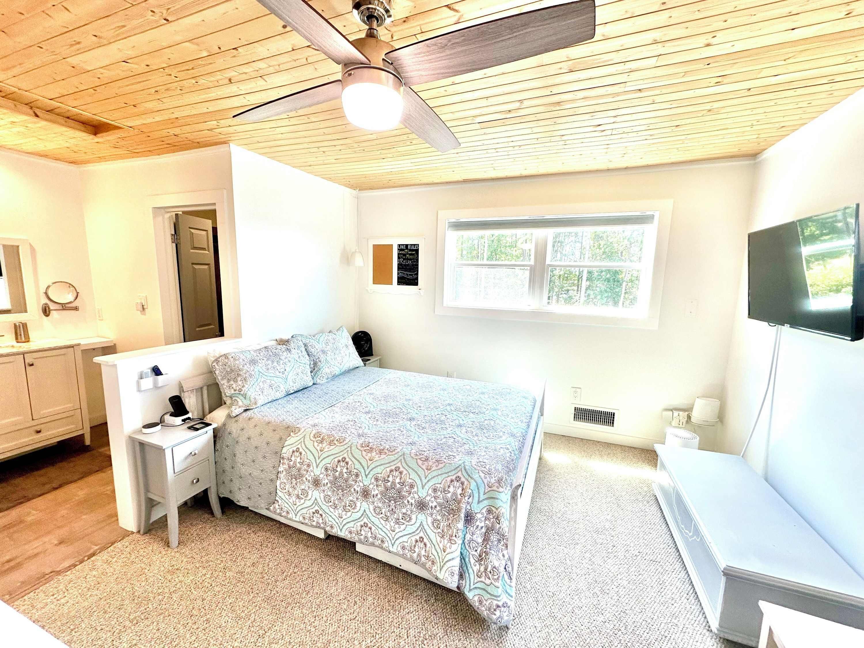 A bedroom with a bed, a nightstand, a dresser, a ceiling fan, a window, and a TV.
