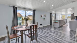 A modern kitchen with a central island, a dining area with a wooden table and chairs, and a view of the outside. - Blue Sky Ranch-walk to beach! Sleeps 6 (Murrells Inlet)
