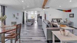 A spacious living area with a wooden dining table, grey sofa, and a kitchen in the background. - Blue Sky Ranch-walk to beach! Sleeps 6 (Murrells Inlet)