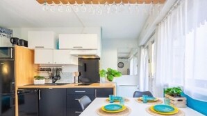 Eine kompakte Küche mit Kühlschrank, Herd und Mikrowelle. Ein Esstisch mit blau-gelben Tellern und Gläsern.