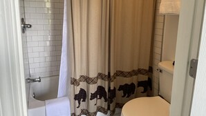 Une salle de bain avec un rideau de douche orné d’un motif d’ours, une baignoire blanche et des toilettes.