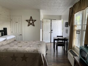 Une chambre à coucher comprenant un lit, un bureau, une chaise, un radiateur et une fenêtre avec des rideaux.