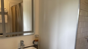 Une salle de bain avec un lavabo blanc, un miroir et un verre contenant un liquide ambré, posé sur le mur.