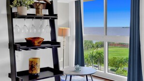 Una habitación con vista al mar, una estantería con copas de vino, una lámpara y una pequeña mesa.