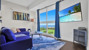 Una sala de estar moderna con un sofá azul, una mesa redonda de centro y una pantalla grande de televisor que muestra una escena de playa.